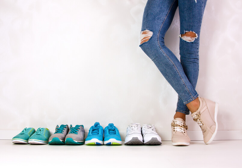A sporty girl in jeans chooses which sneakers to go for training Several pairs of sports shoes and legs